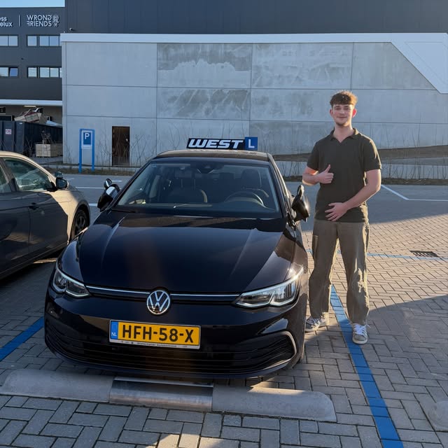 Geslaagde leerling poseert na het behalen van zijn rijbewijs bij de WEST-lesauto