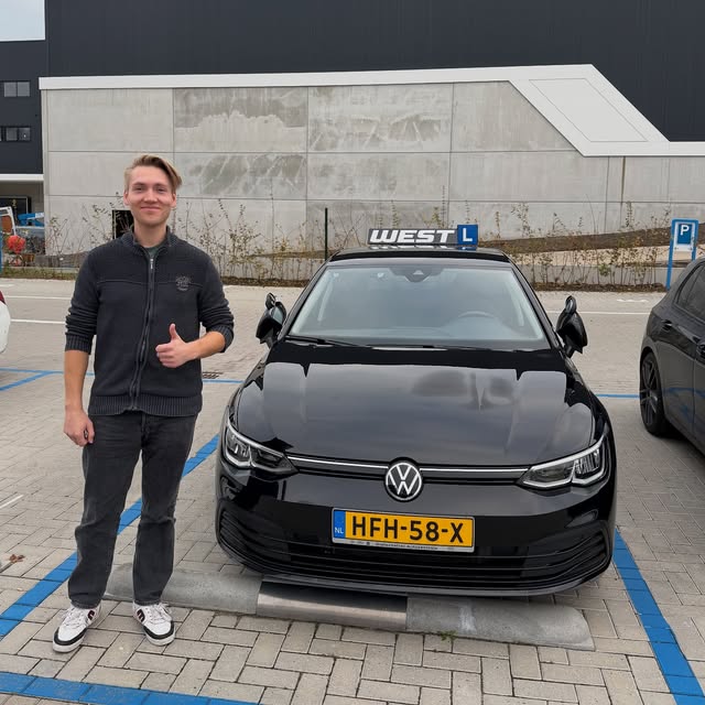 Geslaagde leerling staat na zijn examen naast de WEST-lesauto